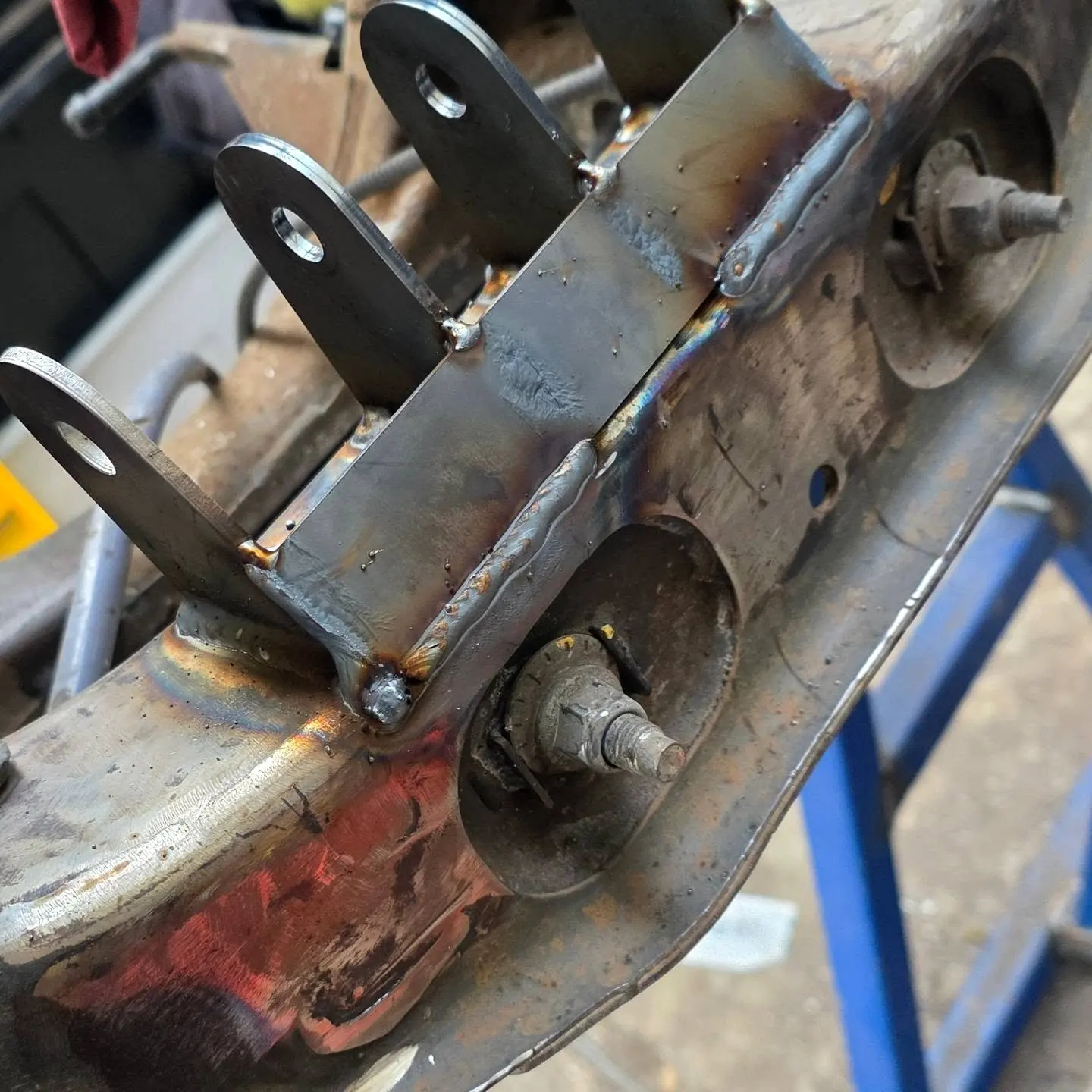Fresh welds on a steel bracket on a car's rear cradle, showing the weld runs and heat colour
