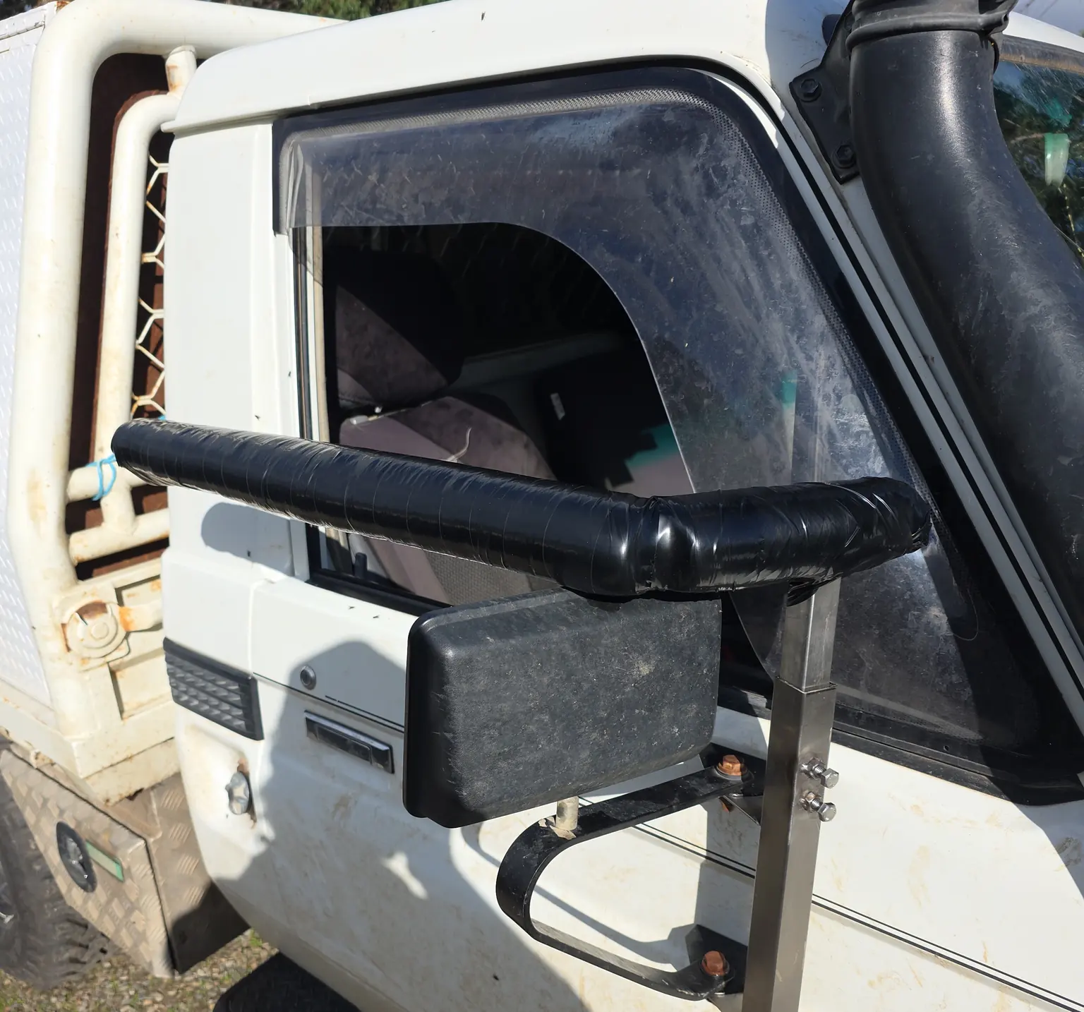 Steel bracket bolted to the door of a white four-wheel drive, holding the side mirror