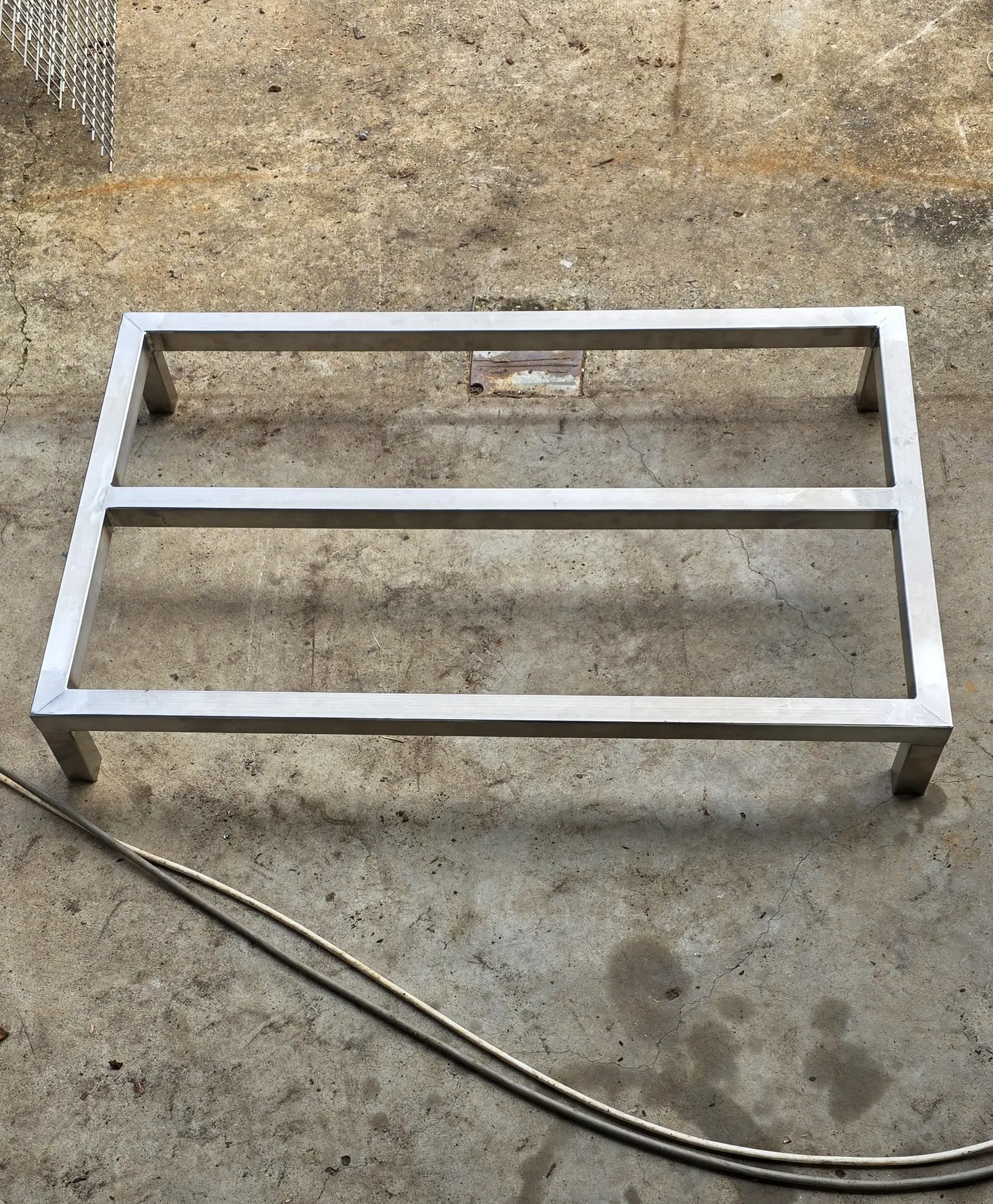 Stainless steel stand frame on a concrete workshop floor, with a welding lead beside it