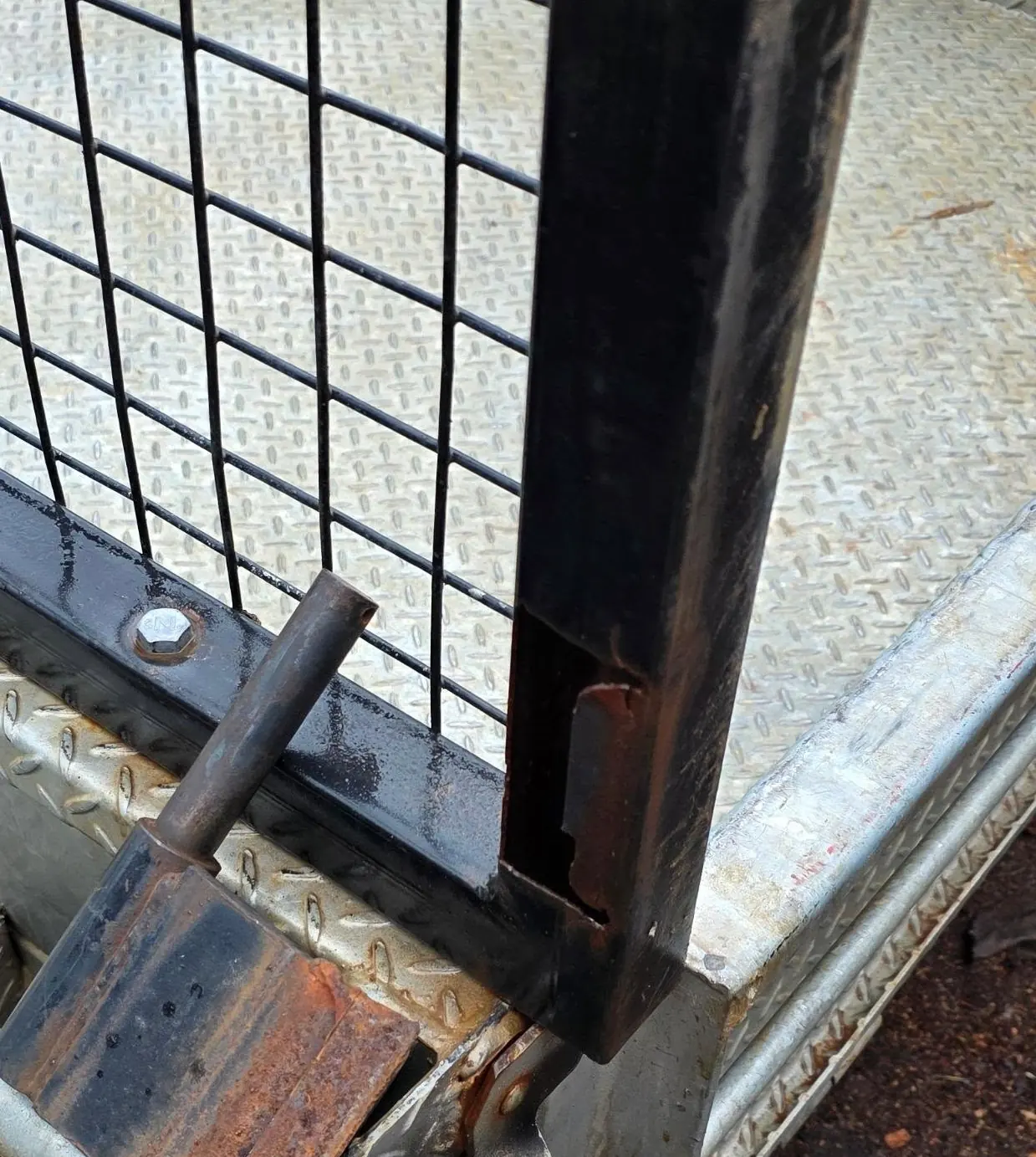 Trailer cage gate upright cracked around the weld, with rust at the hinge